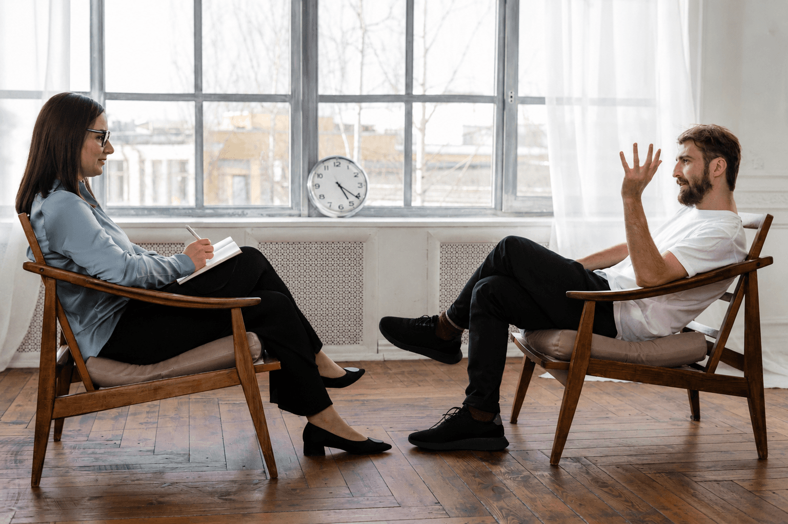 A patient and clinician seated in matching chairs during a daylit therapy session
