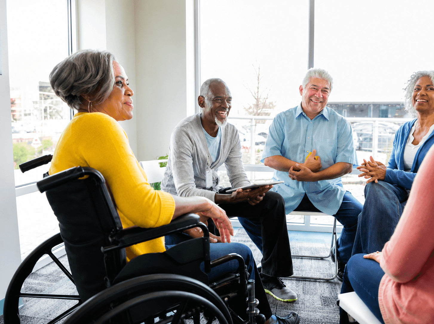 A welcoming group conversation including a woman in a wheelchair, mid-laugh